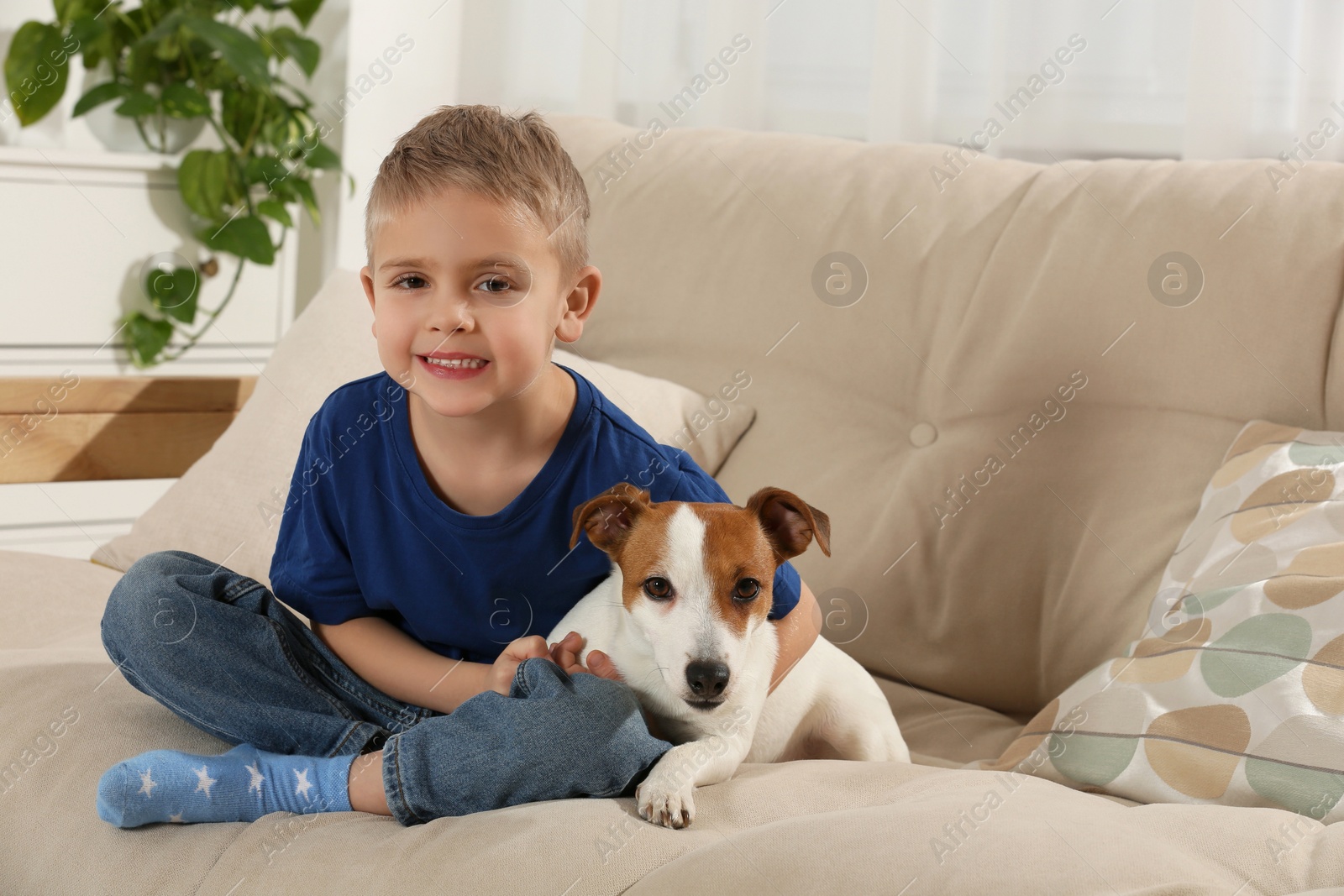 Photo of Little boy with his cute dog on sofa at home, space for text. Adorable pet