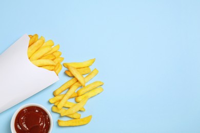 Paper cup with French fries and ketchup on light blue table, flat lay. Space for text