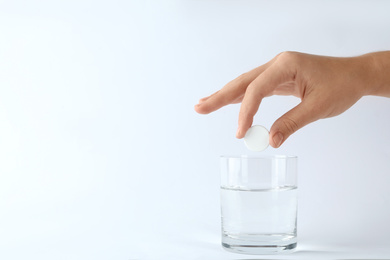 Woman putting tablet into glass of water on white background, space for text