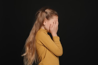 Photo of Girl covering face with hands on black background. Children's bullying