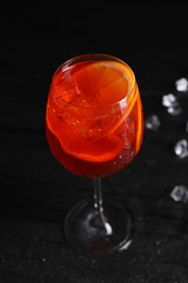 Photo of Glass of tasty Aperol spritz cocktail with ice cubes on table against black background