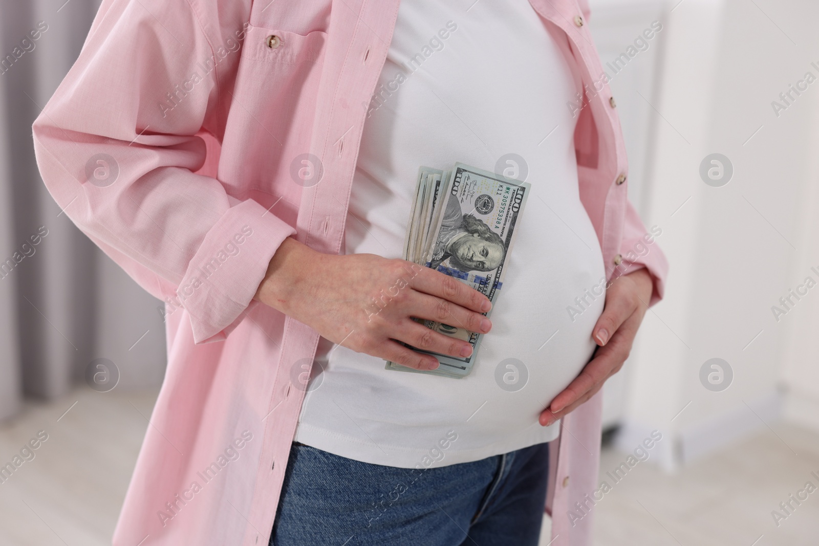 Photo of Surrogate mother. Pregnant woman with dollar banknotes indoors, closeup