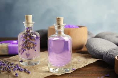 Photo of Bottles with natural herbal oil and lavender flowers on table against blurred background
