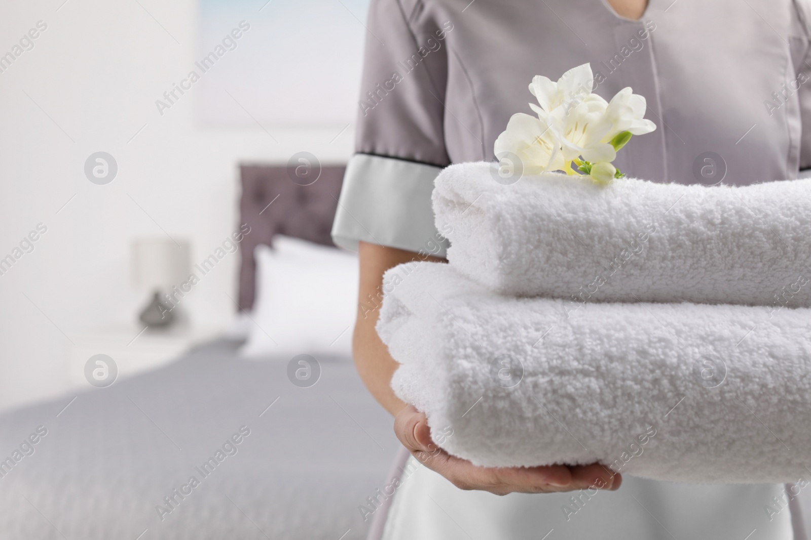 Photo of Maid holding fresh towels with flowers in hotel room, closeup