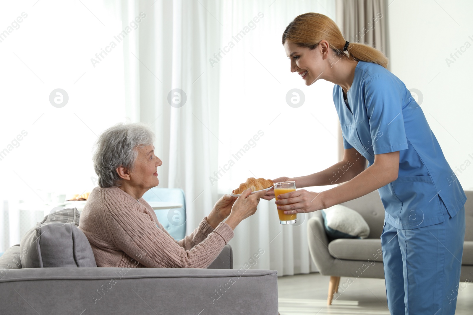 Photo of Nurse serving breakfast to elderly woman indoors. Assisting senior people