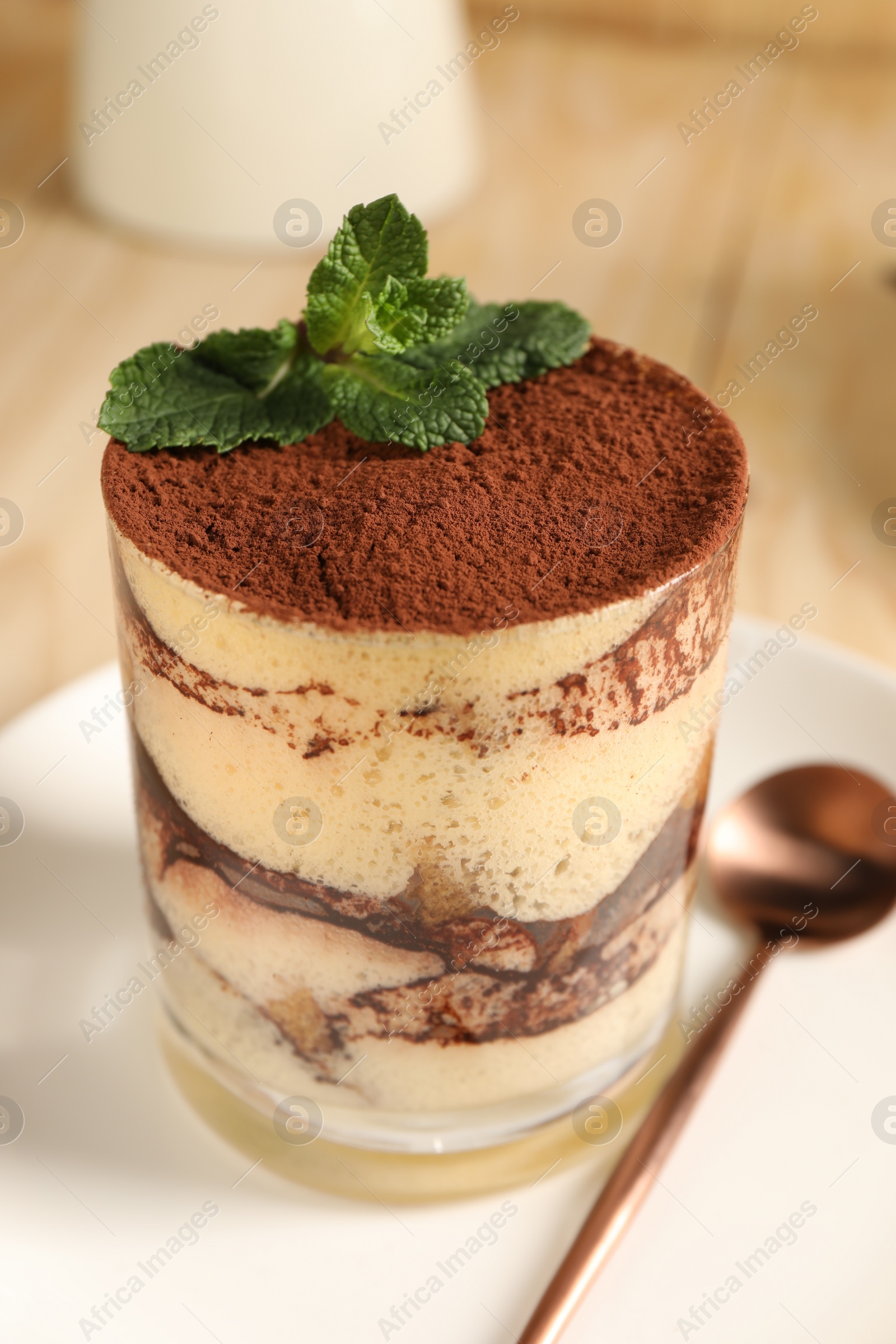 Photo of Tasty tiramisu and mint in glass on table, closeup