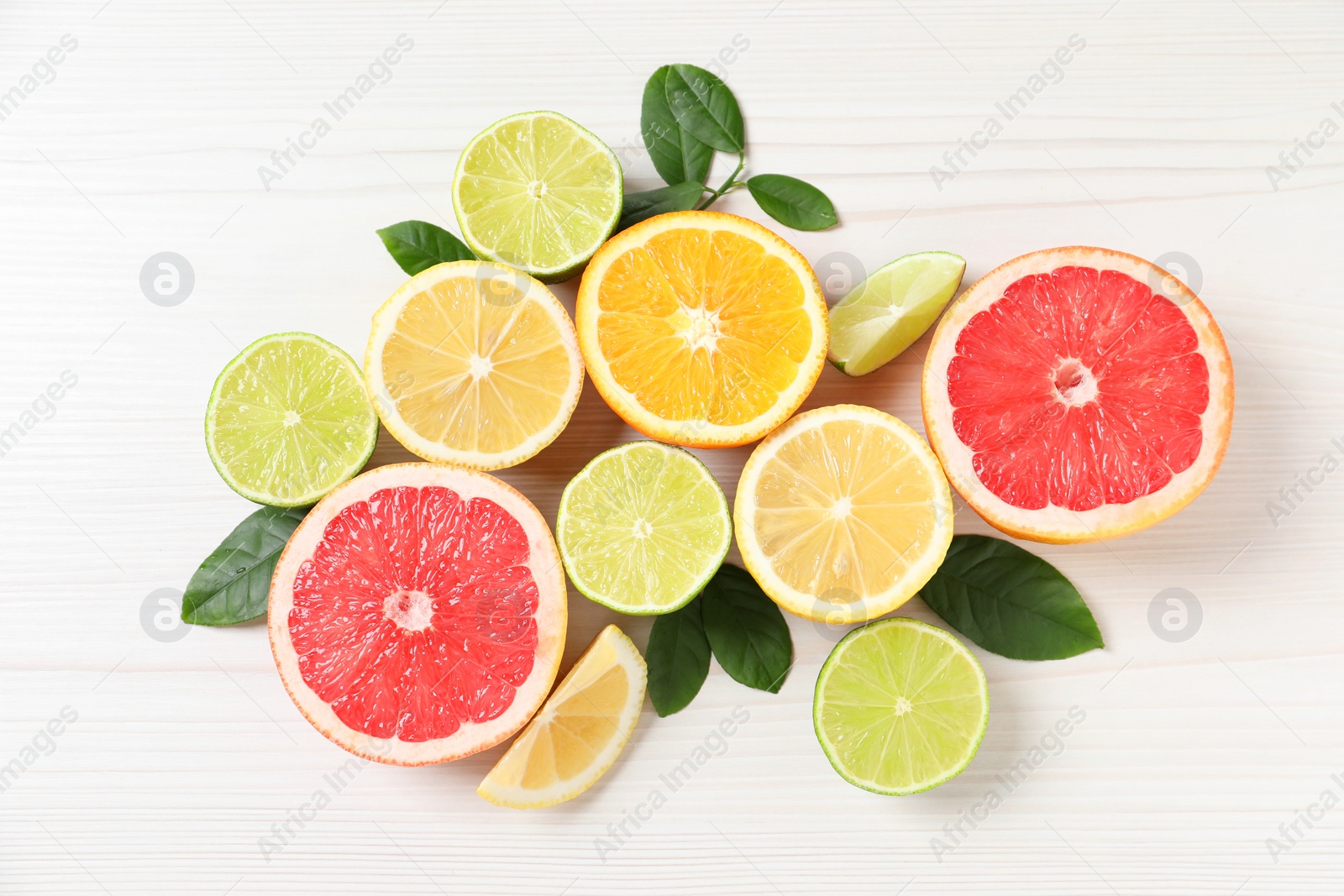 Photo of Different cut citrus fruits and leaves on white wooden table, flat lay