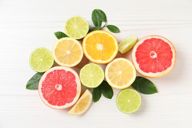 Photo of Different cut citrus fruits and leaves on white wooden table, flat lay