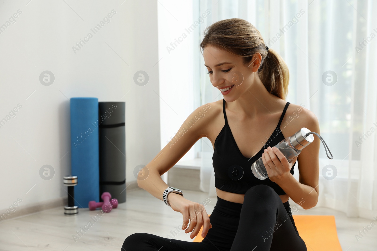 Photo of Young woman using smart watch during training indoors