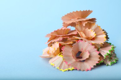 Photo of Pile of colorful pencil shavings on light blue background, closeup. Space for text