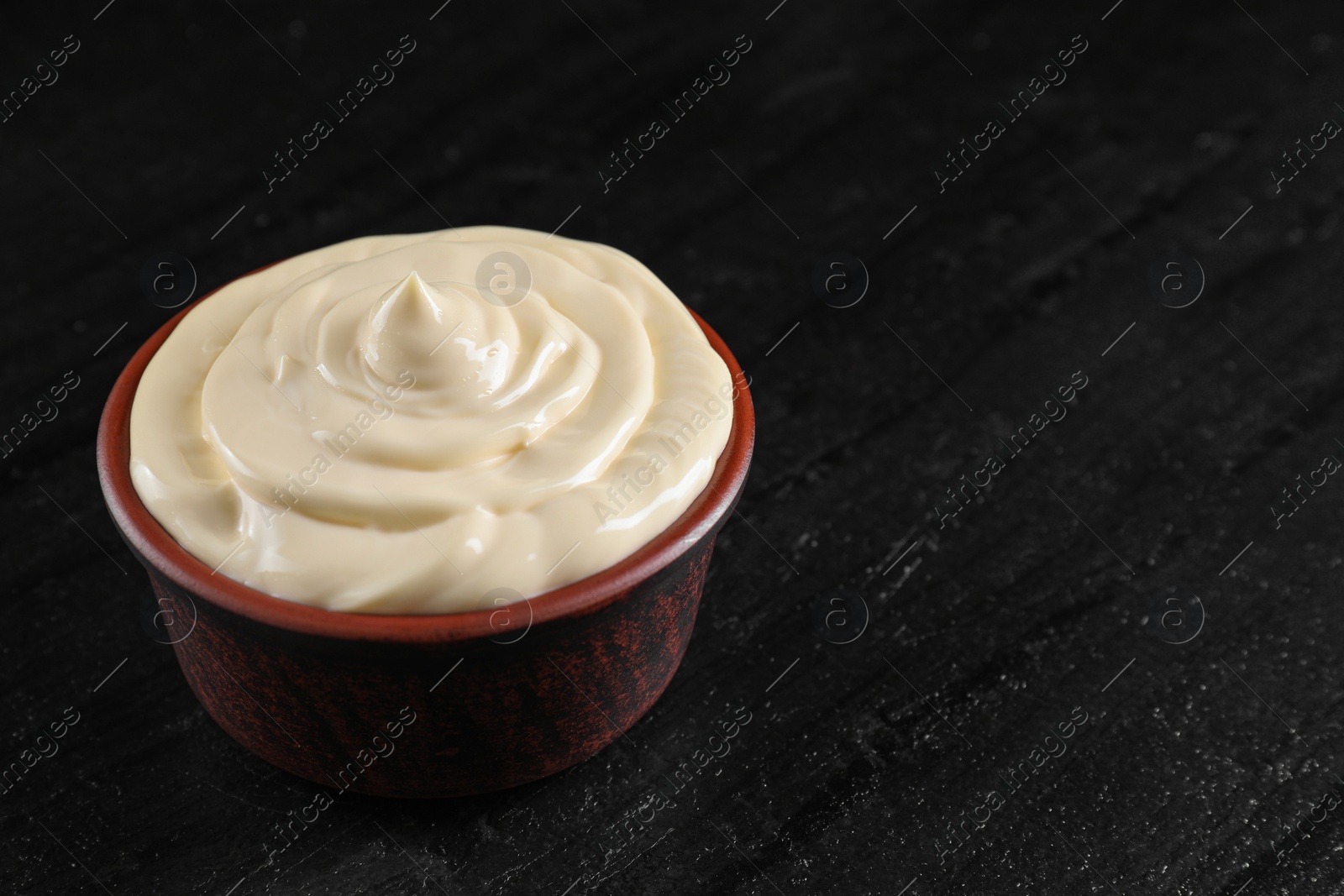 Photo of Fresh mayonnaise sauce in bowl on black table, closeup. Space for text