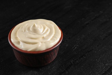 Photo of Fresh mayonnaise sauce in bowl on black table, closeup. Space for text