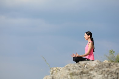 Photo of Young woman meditating on cliff. Space for text