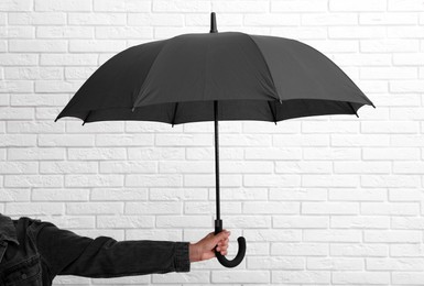 Photo of Woman with open black umbrella near white brick wall, closeup