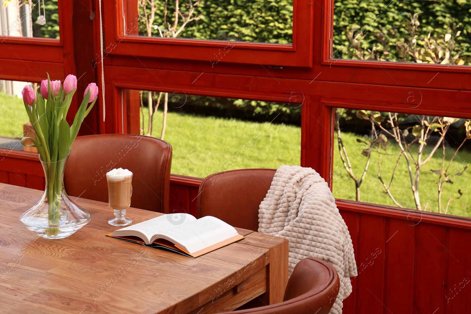 Photo of Glass of delicious cocoa, pink tulips and book on wooden table at terrace