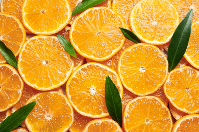 Slices of fresh ripe tangerines and leaves as background, top view. Citrus fruit