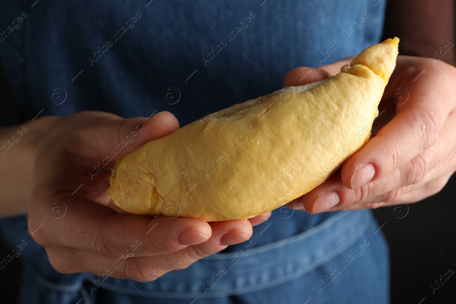 Photo of Woman holding piece of durian on dark background, closeup