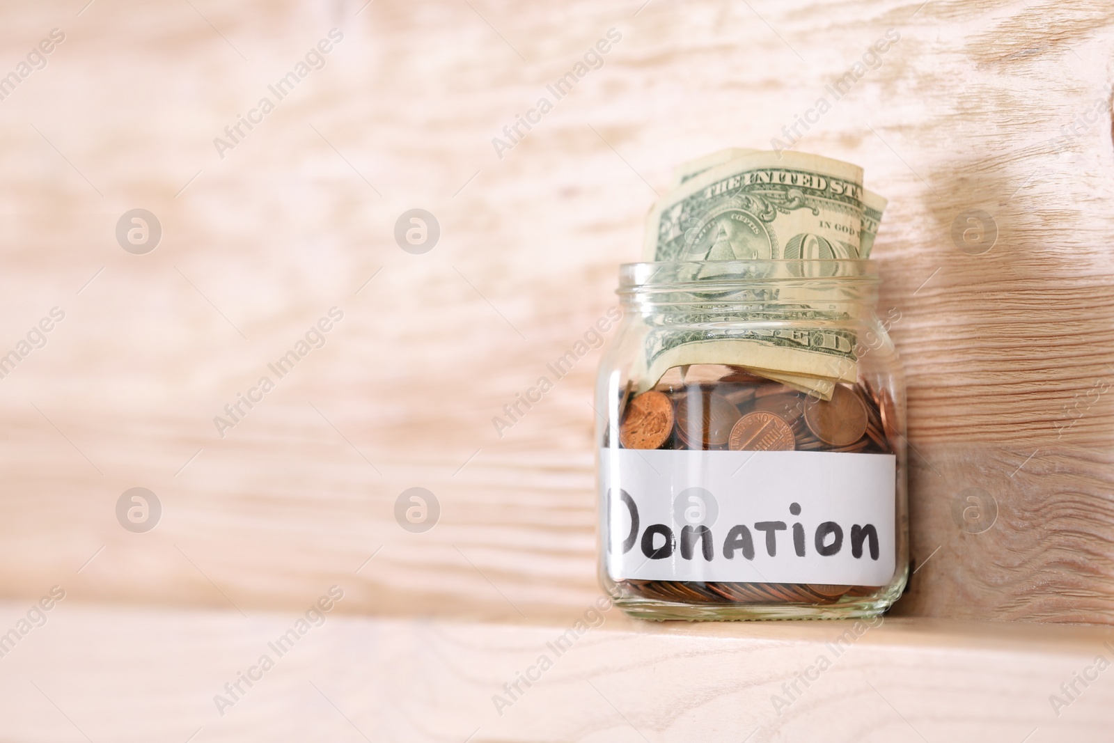 Photo of Glass jar with money and label DONATION on shelf against wooden background. Space for text