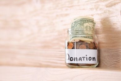 Photo of Glass jar with money and label DONATION on shelf against wooden background. Space for text