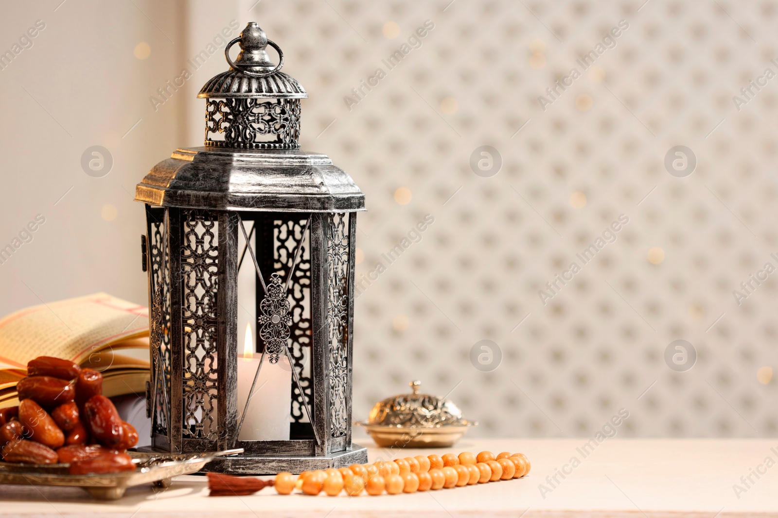 Photo of Arabic lantern, Quran, misbaha and dates on white table. Space for text