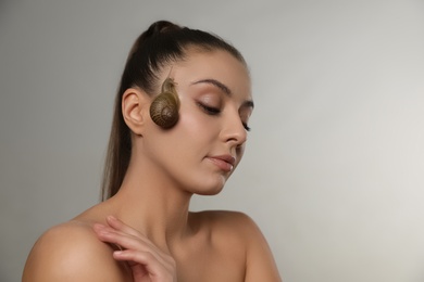 Photo of Beautiful young woman with snail on her face against grey background. Space for text