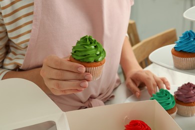 Woman holding delicious cupcake with green cream at table indoors, closeup