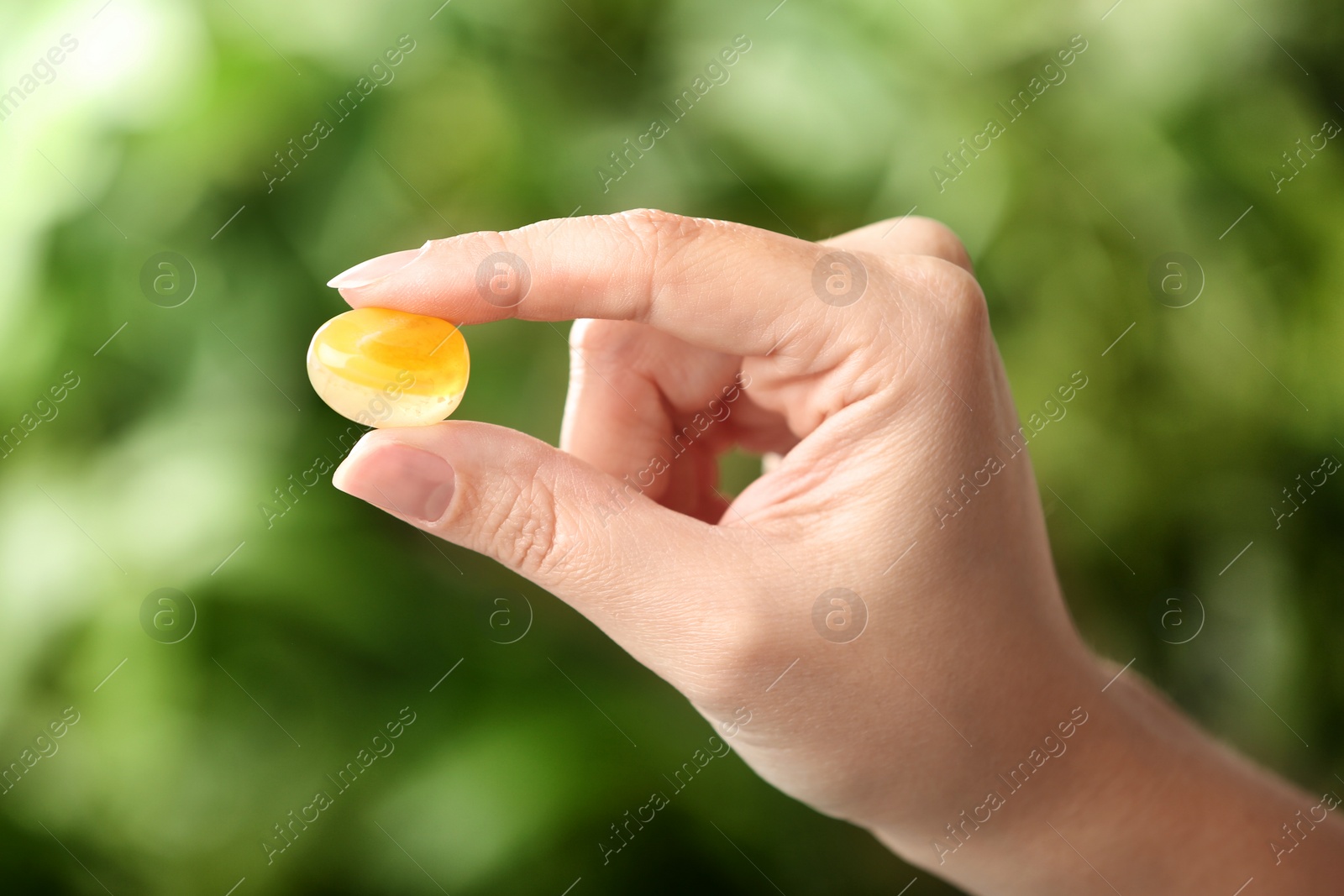 Photo of Woman holding beautiful honey agate gemstone on blurred green background, closeup