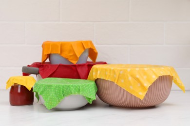 Photo of Different dishware covered with beeswax food wraps on white marble table