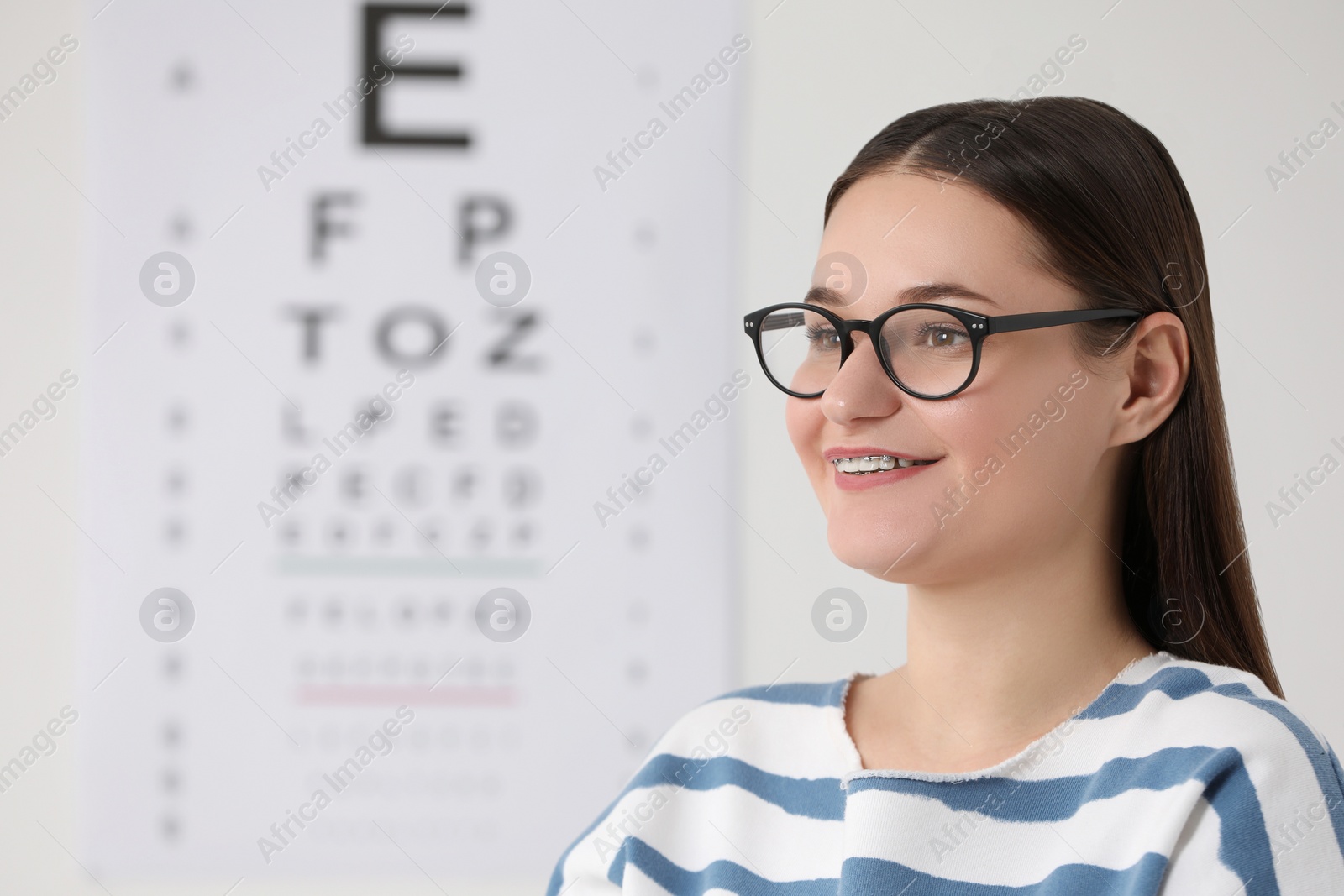 Photo of Young woman with glasses against vision test chart