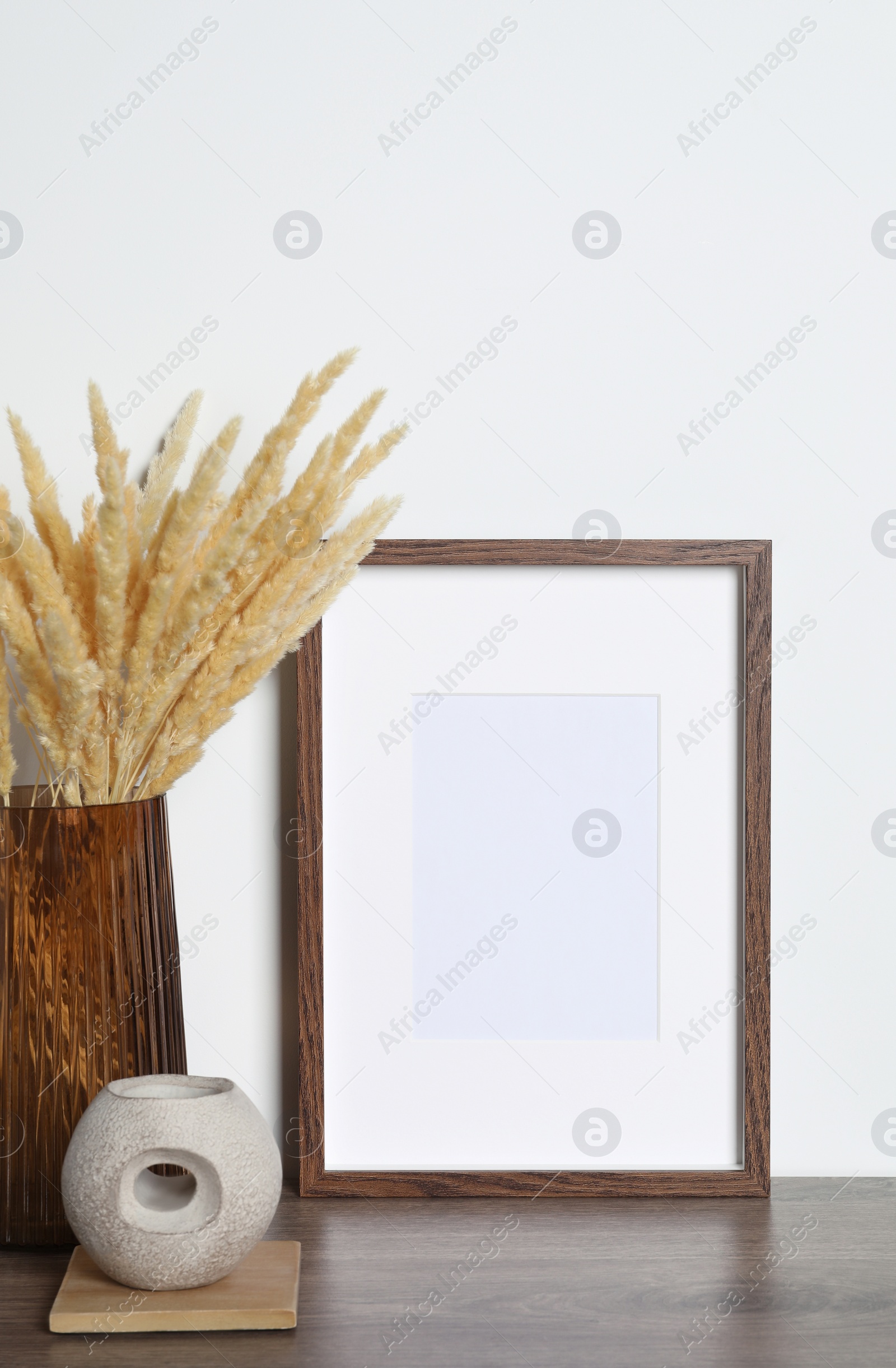 Photo of Empty photo frame and vase with dry decorative spikes on wooden table. Mockup for design