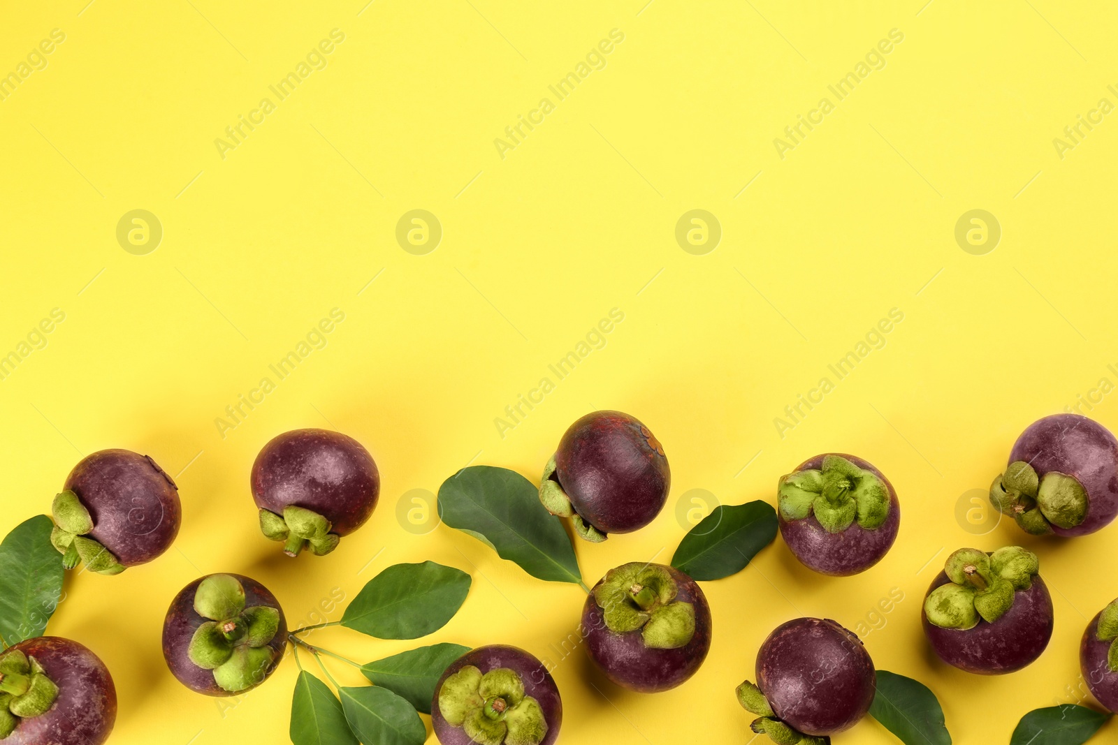 Photo of Fresh ripe mangosteen fruits with green leaves on yellow background, flat lay. Space for text