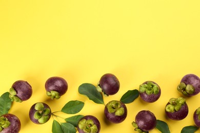 Fresh ripe mangosteen fruits with green leaves on yellow background, flat lay. Space for text