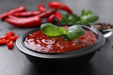 Photo of Bowl of chili sauce with basil leaves on grey table, closeup