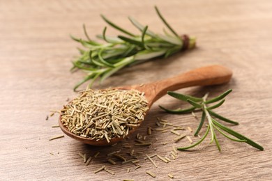 Photo of Spoon with dry rosemary and fresh twigs on wooden table, closeup