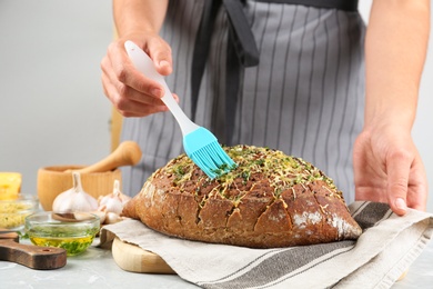 Photo of Woman brushing tasty homemade bread with garlic and herbs at light table, closeup