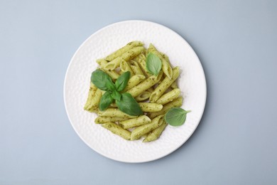 Delicious pasta with pesto sauce and basil on light grey background, top view