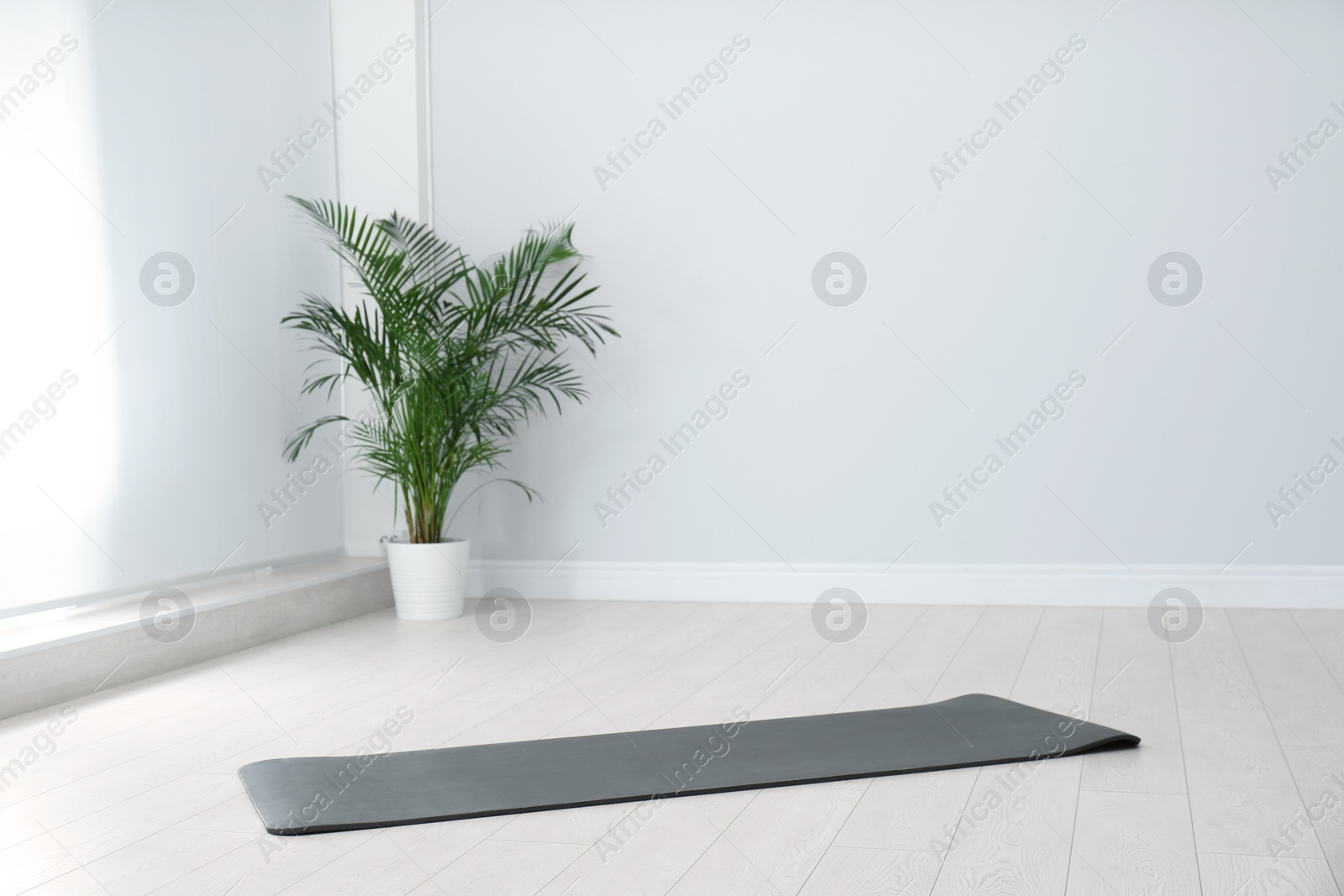 Photo of Unrolled black yoga mat on floor in room. Space for text