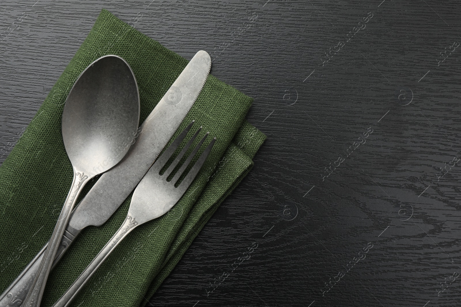 Photo of Stylish setting with cutlery and napkin on black wooden table, top view. Space for text