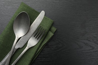 Stylish setting with cutlery and napkin on black wooden table, top view. Space for text