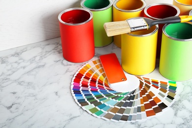 Photo of Cans with paint, brush and color palette on marble table