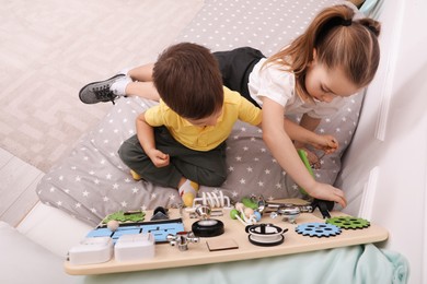 Photo of Little boy and girl playing with busy board on bed in room, above view