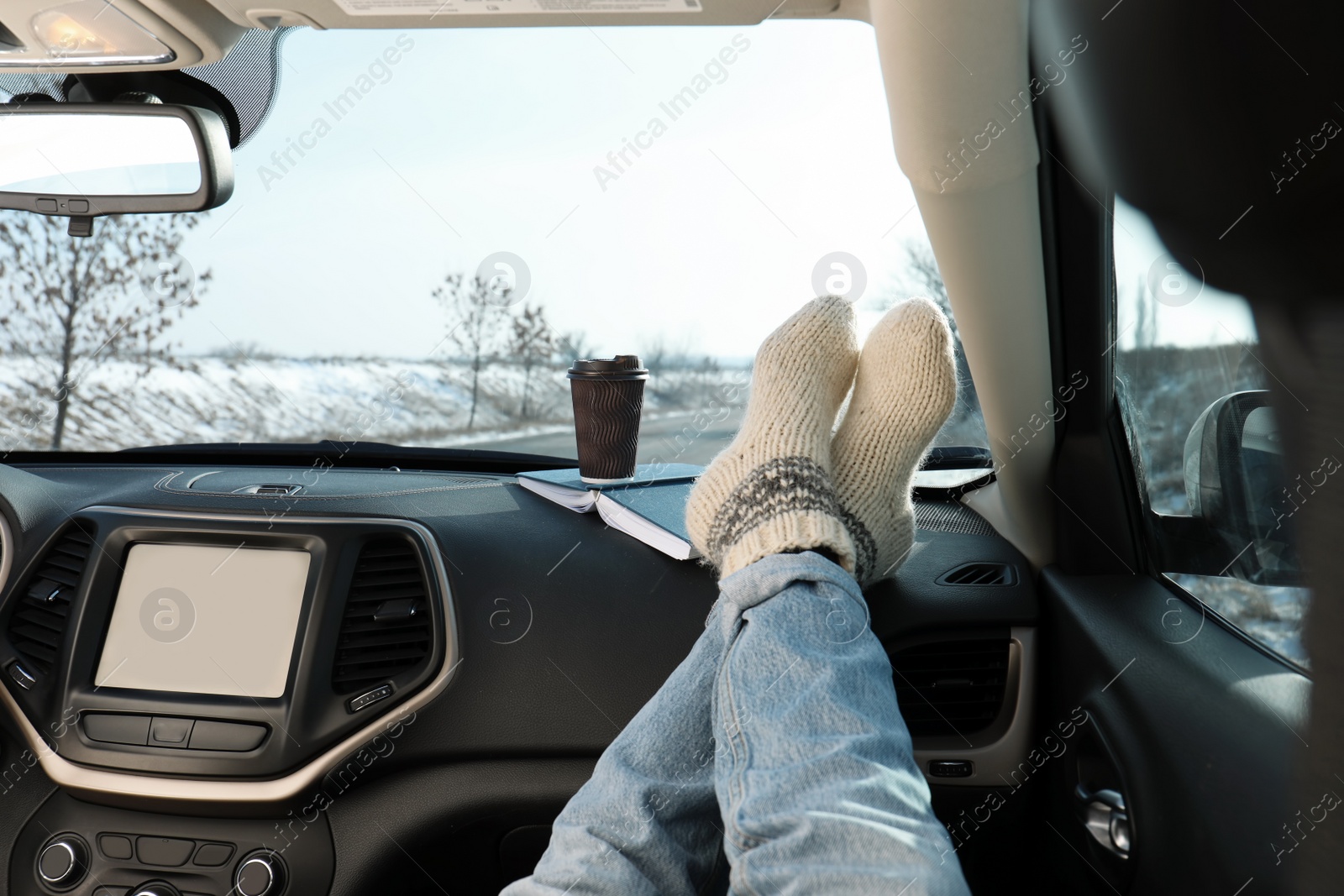 Photo of Young woman in warm socks holding her legs on car dashboard. Cozy atmosphere