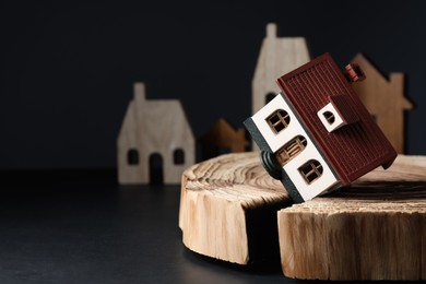Photo of House model in cracked wooden stump on black table depicting earthquake disaster. Space for text