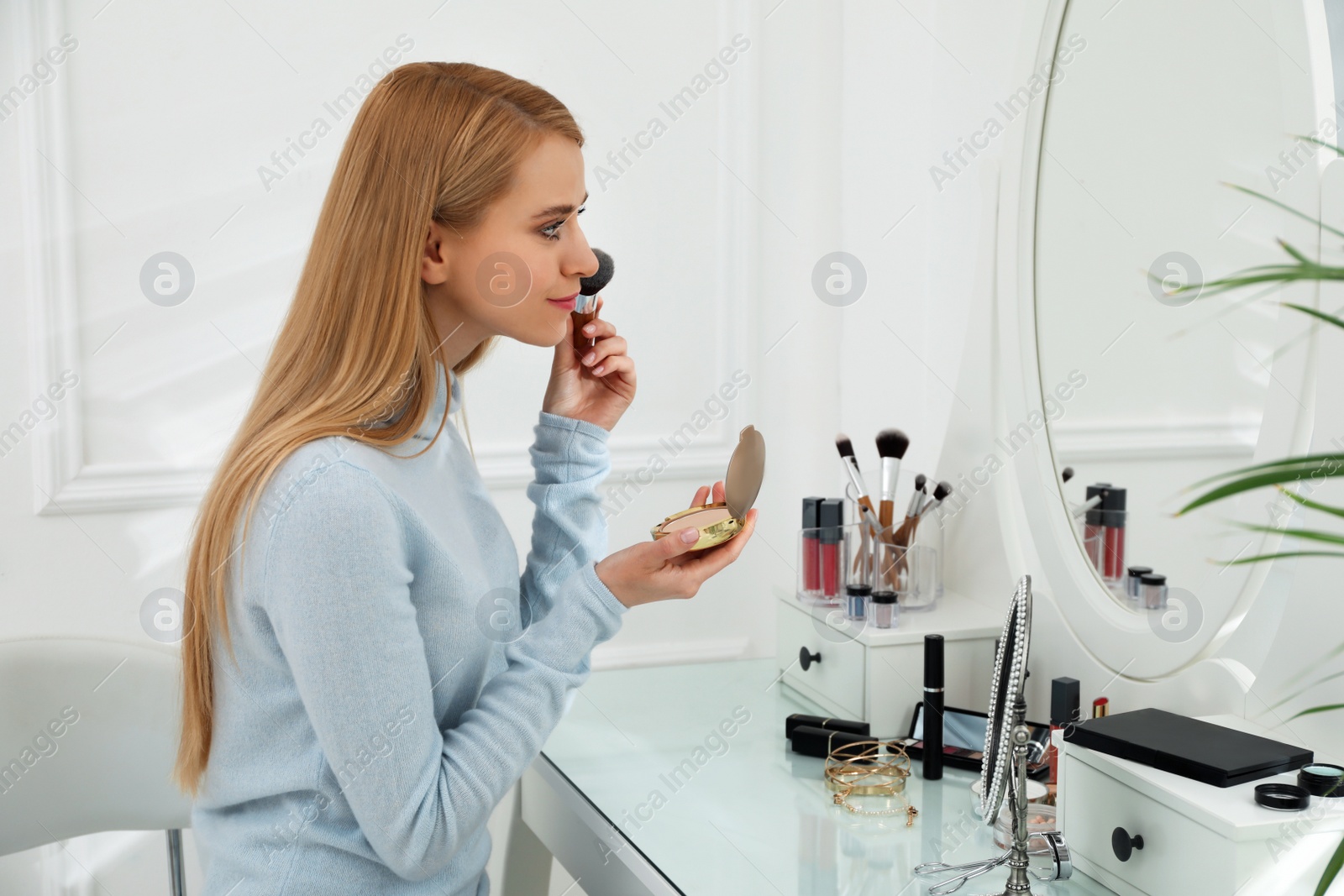 Photo of Beautiful woman applying makeup near mirror in room