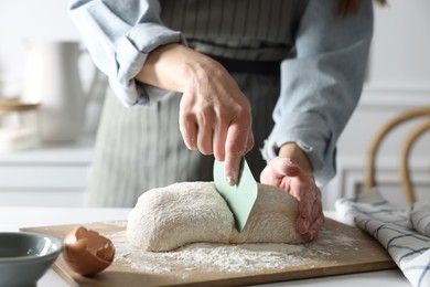 Photo of Woman cutting dough at white wooden table in kitchen, closeup