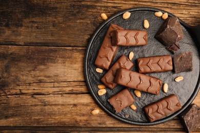 Photo of Slate board of chocolate bars with nuts and pieces on wooden table, top view. Space for text