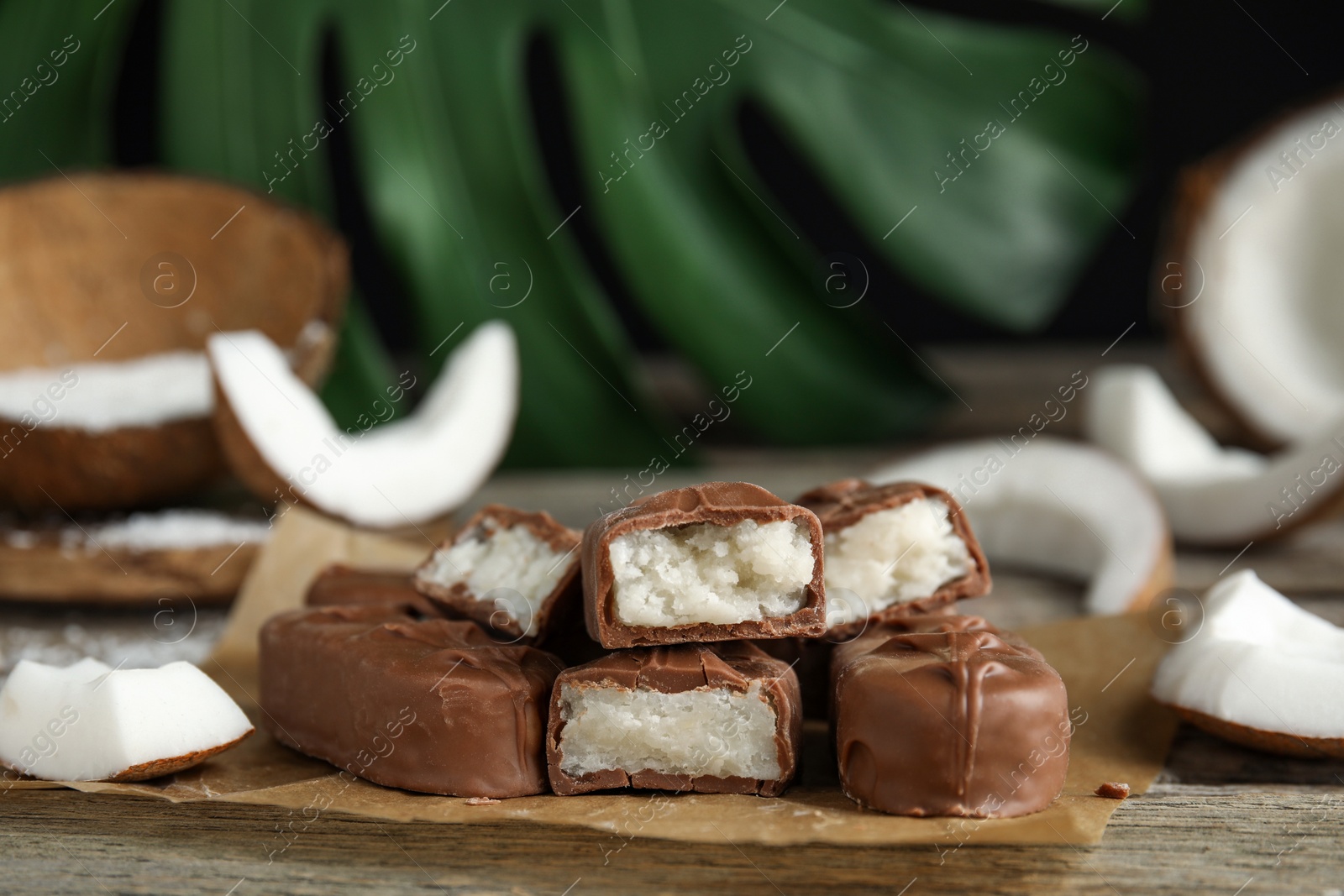 Photo of Delicious milk chocolate candy bars with coconut filling on wooden table, closeup. Space for text