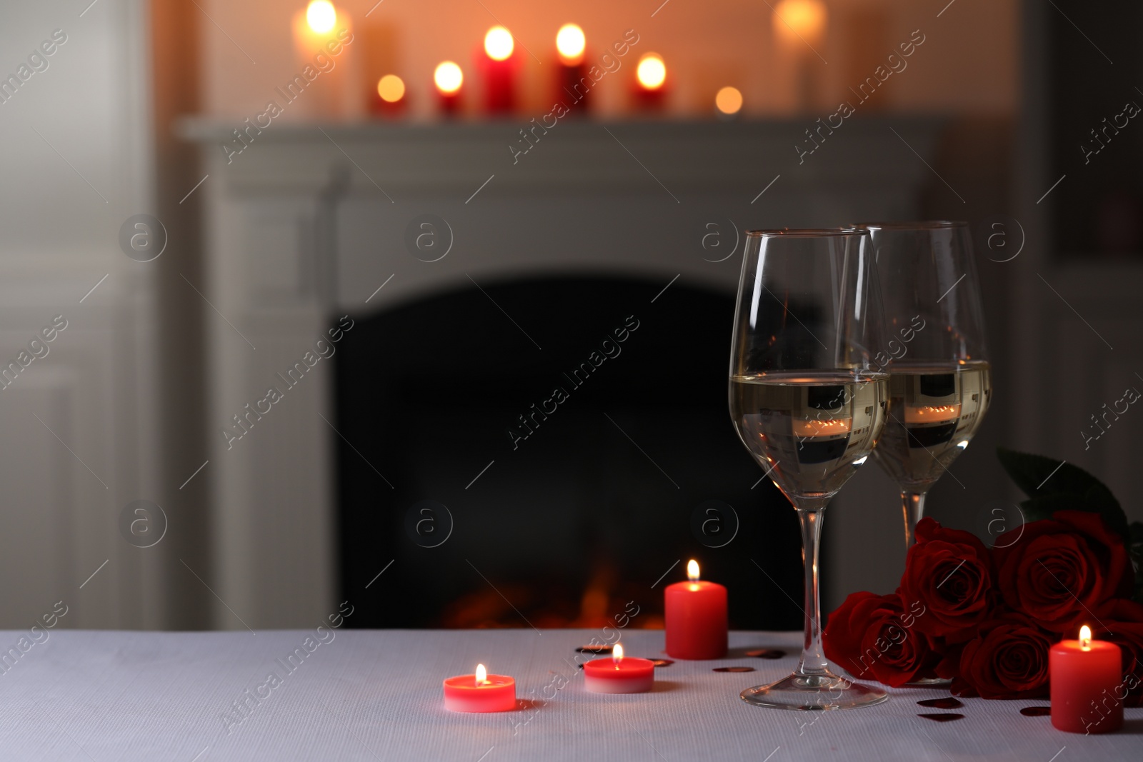 Photo of Glasses of white wine, rose flowers and burning candles on grey table indoors, space for text. Romantic atmosphere