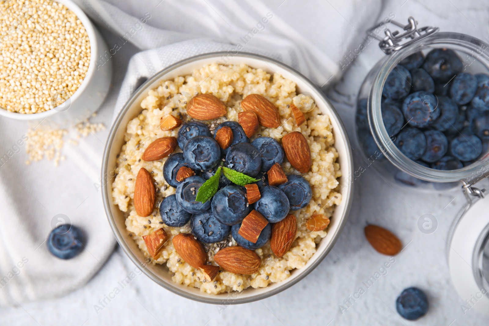 Photo of Bowl of delicious cooked quinoa with almonds and blueberries on white textured table, flat lay