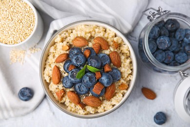 Bowl of delicious cooked quinoa with almonds and blueberries on white textured table, flat lay